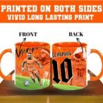 Two orange mugs featuring Memphis basketball artwork, shown front and back with bold team graphics against a stadium backdrop.